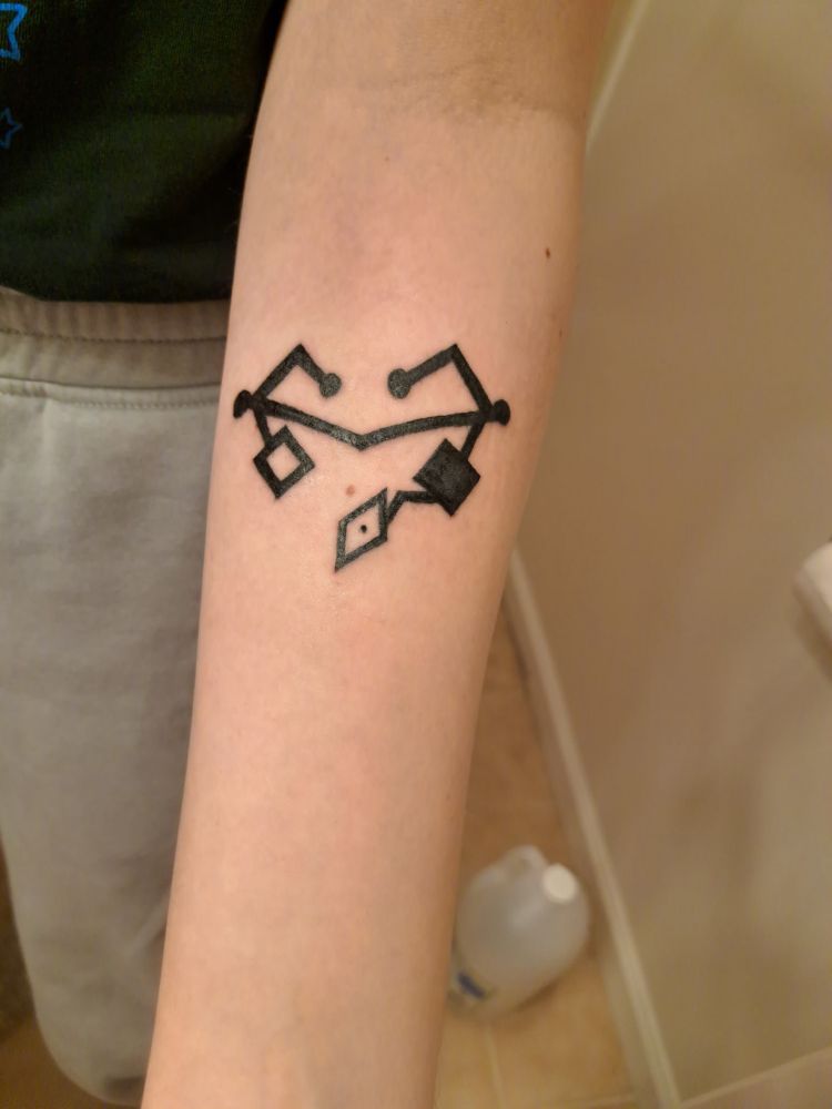 A photo of Glimmer’s inner forearm. A black ink tattoo of the “heart” symbol from She-Ra and the Princesses of Power finale is visible. 