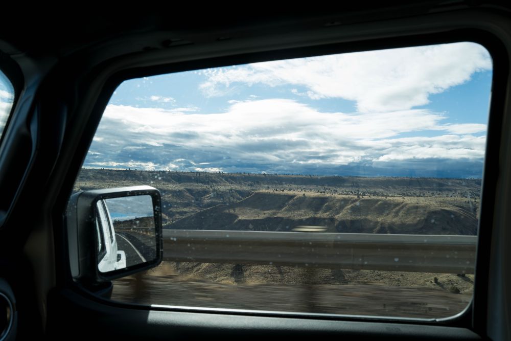 A black and white photo of a canyon framed through a vehicle’s passenger-side window. 