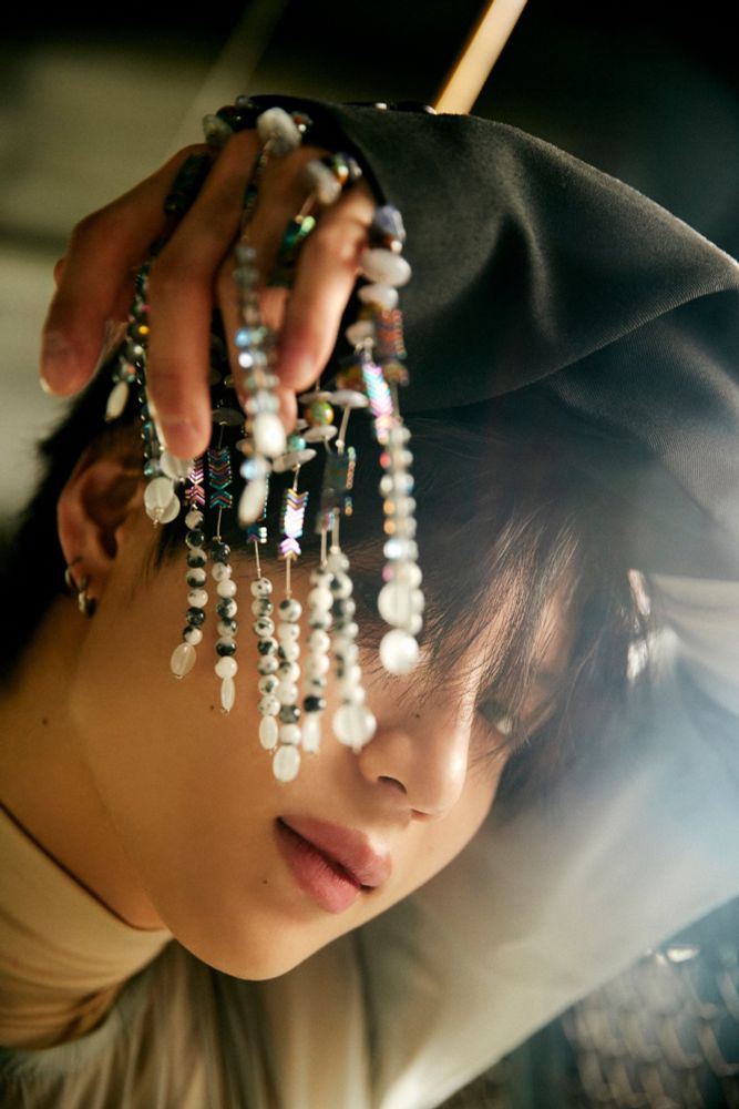 Taemin with his left arm curved over his head and multiple strands of beads dangling from his hand. He’s staring at the camera with lips slightly parted 
