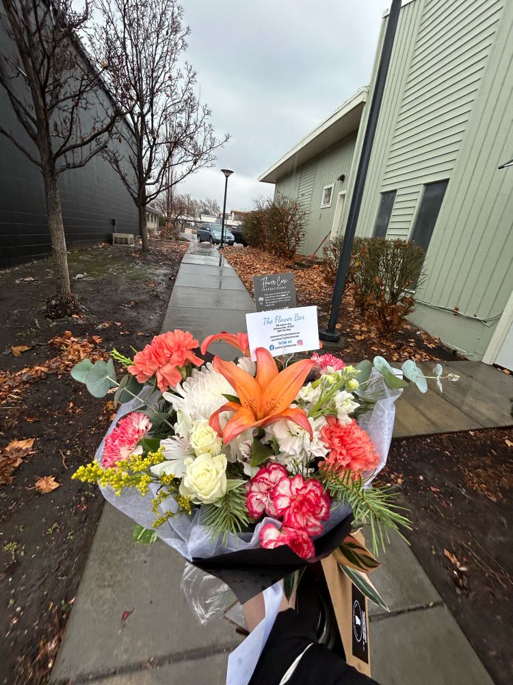 A bouquet of white, red, and peach colored flowers. In the background there is a wet sidewalk and buildings 