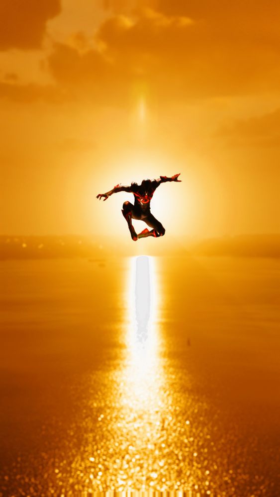 A screenshot from the video game Spider-Man 2 for the PlayStation 5. Spider-Man is seen leaping over a shimmering ocean as the sun sets directly behind him. He is posed in a way to show his jump, with light highlighting the red accents of his suit. His face is hidden by shadow. His suit's design is the Tokusatsu suit.