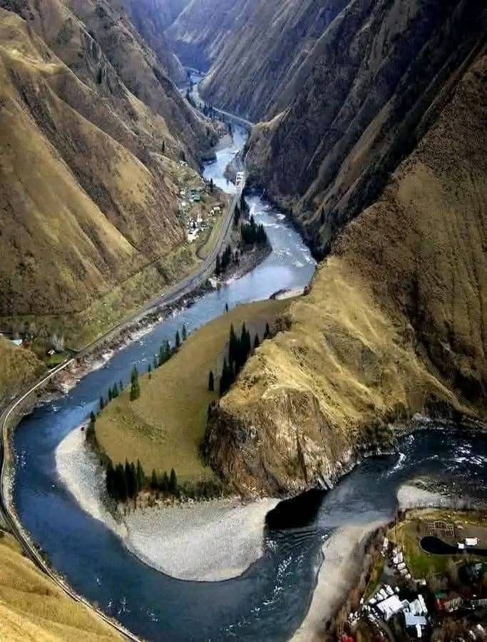 A drone photo of the Salmon River. Blue winding waters, white sandy beaches, a single 2-lane road winding along the left bank. The river is surrounded by steep treeless slopes. 