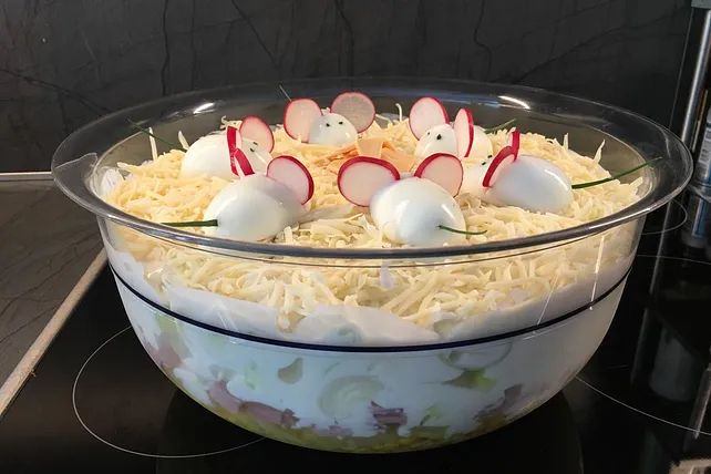 Ein Schichtsalat mit gekochten Eiern oben drauf, die in Mäuse verwandelt wurden mit Radieschen Ohren