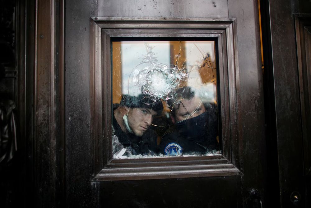 Capitol police officers looking through a shattered window. 