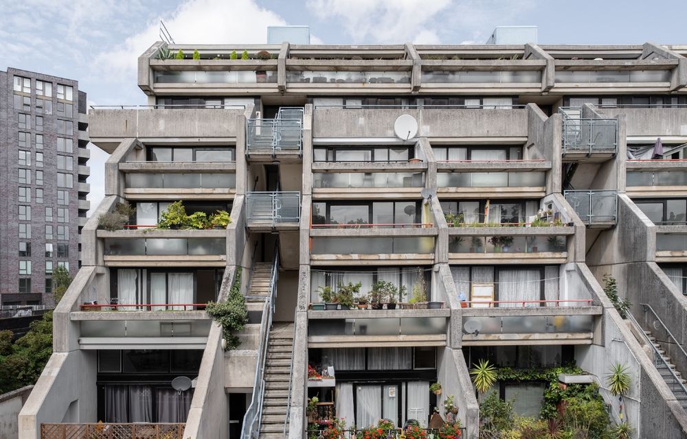 Fronts of a set of brutalist estate homes, stepped back so each has an open terrace, many covered with plants