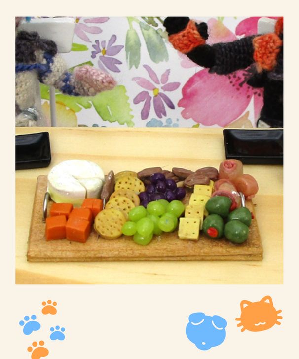 Custom made Altare and Axel plushies, mostly cropped out of the polaroid image, are sitting at a table drinking latte's while snacking in a charcuterie board filled with fruits, cheeses and crackers