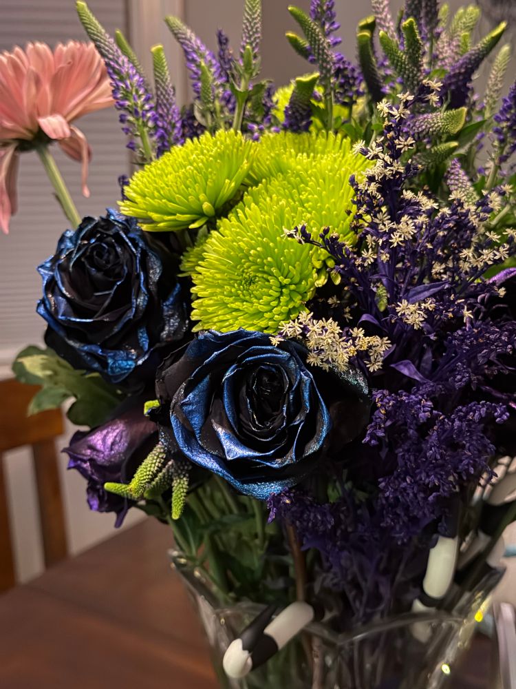 Colorful flower arrangement in a crystal vase containing purple and deep blue pearlescent roses, neon green chrysanthemums and lilac (I think. I suck at identifying flowers)