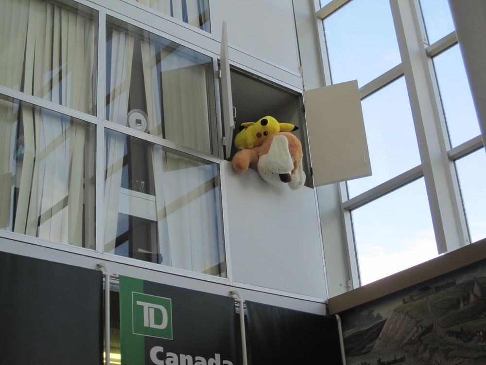 A stuffed Pikachu is pushing another stuffed animal out of a second floor window.