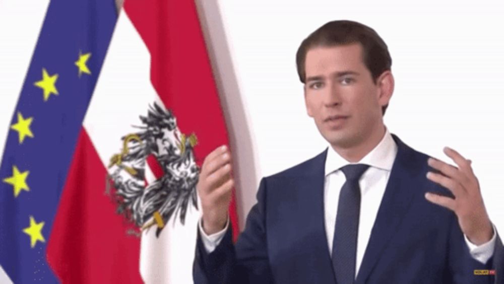 a man in a suit and tie stands in front of a flag that says austria