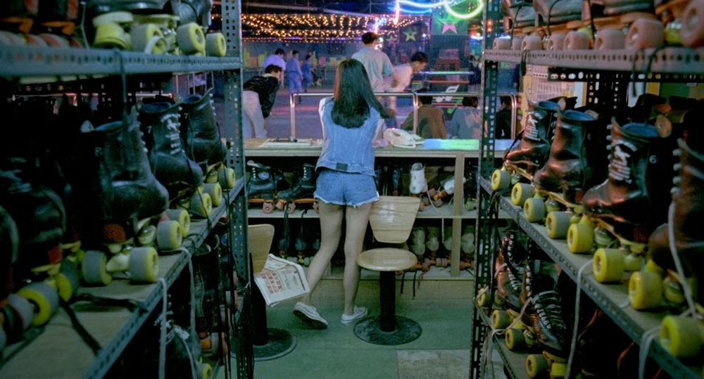 a still from Rebels of the Neon God (1992). A young woman picks up the phone at her skate return desk of a roller rink 