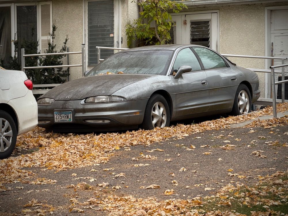 Decrepit-looking Oldsmobile Aurora, sitting in a driveway. 