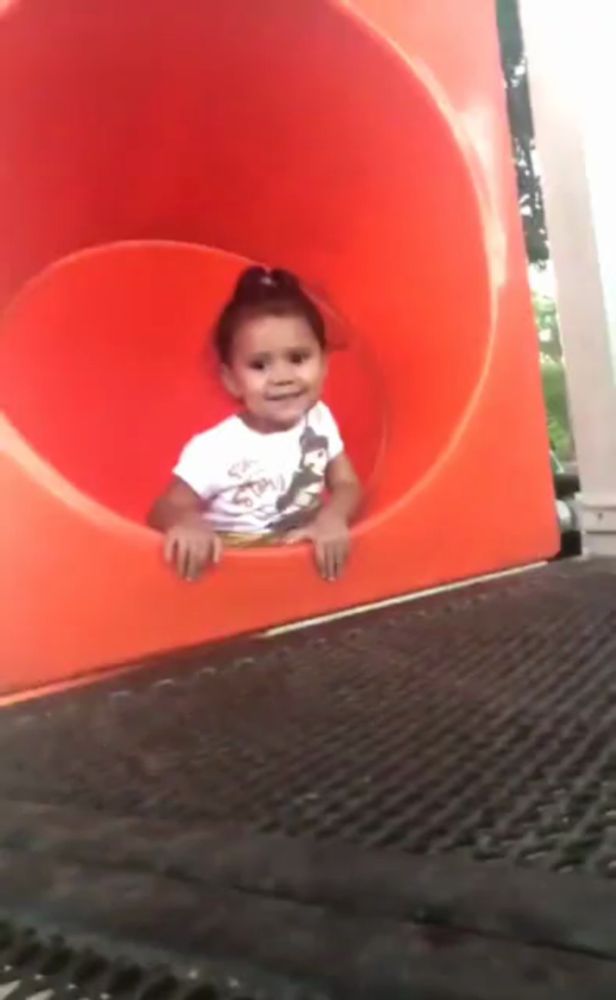 a little girl is going down a red slide at a playground