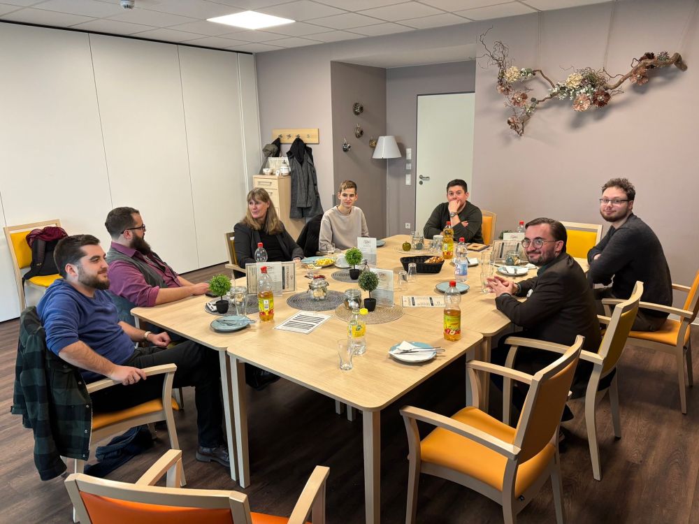 7 Mitglieder sitzen um einen Tisch mit Getränken und diskutieren 