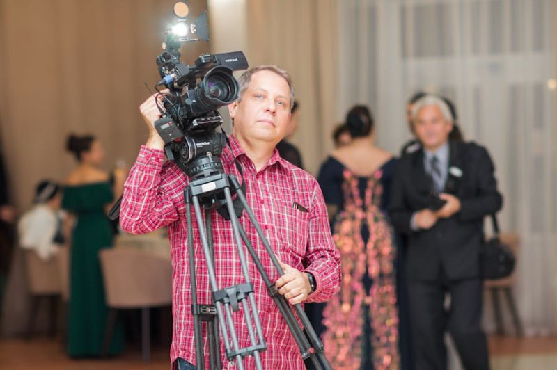 Image of man carrying camera on tripod at a formal event. Image by korso 00007 via Pexels