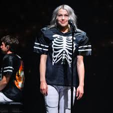 Phoebe Bridgers in concert wearing a black and white football jersey with a skeleton design, with football shoulder pads underneath 