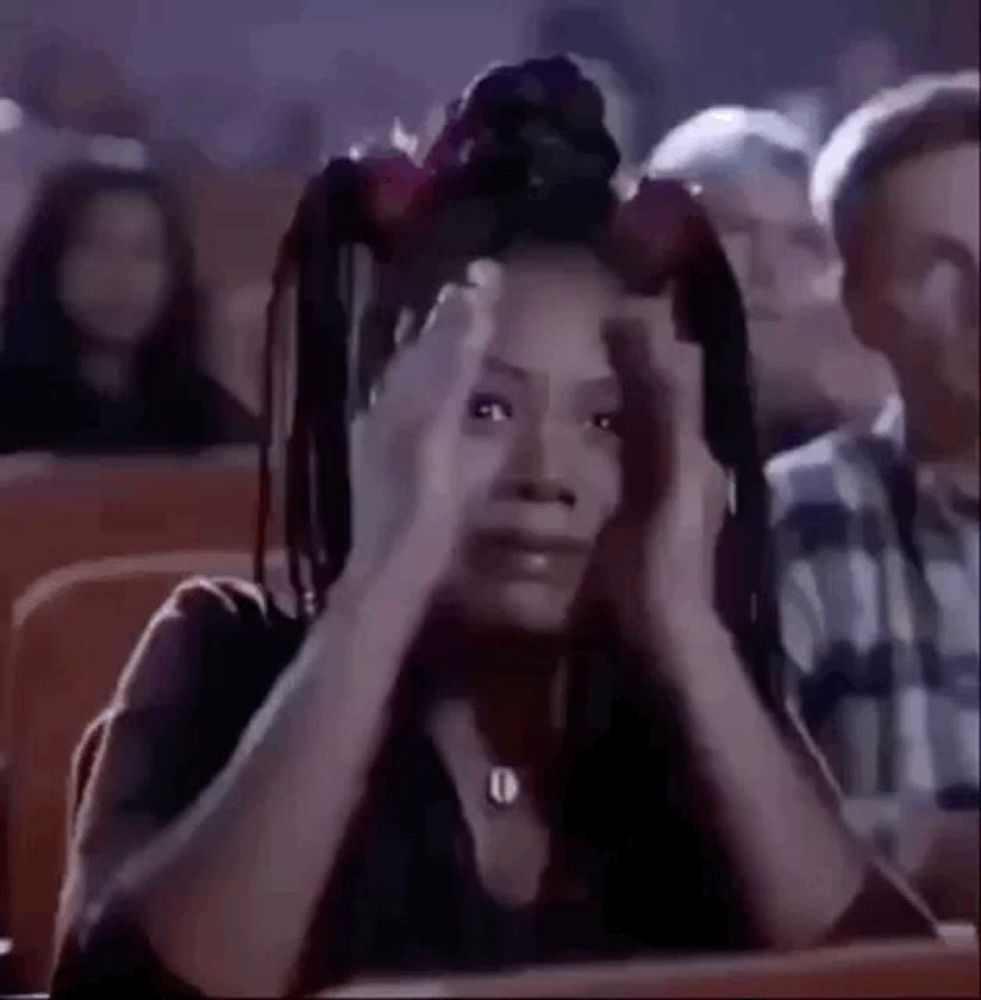 a woman is sitting in a theatre holding her head in pain .