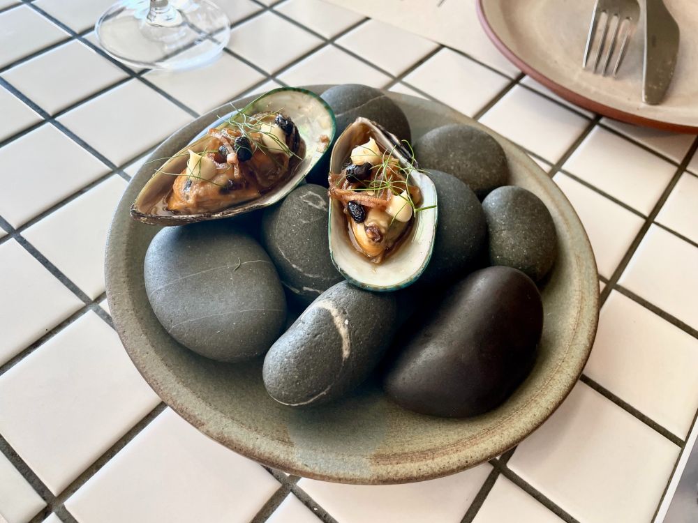 Plate with two mussels on open shell, covered with bits of sauce and herbs.