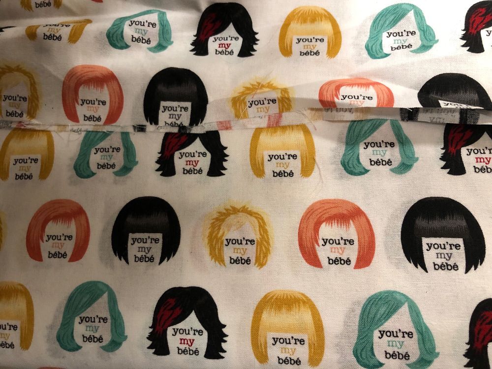 white fabric decorated with different colorful wigs belonging to moira rose with the text reading “you’re my bébé”