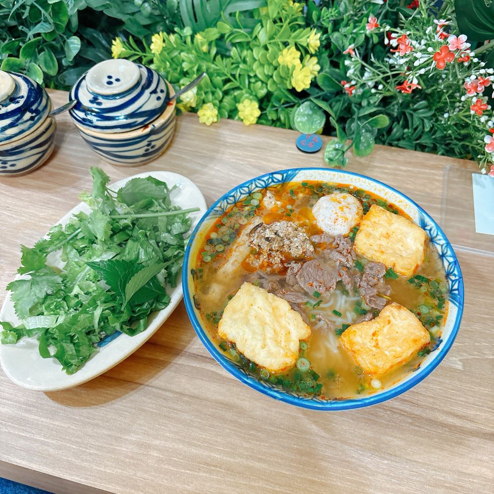 左にパクチーとレタスが山盛りのってるお皿、右にカニ味噌麺のどんぶりがある写真。カニ味噌麺には厚揚げ、薄切り牛肉、つくねなどがのっている。