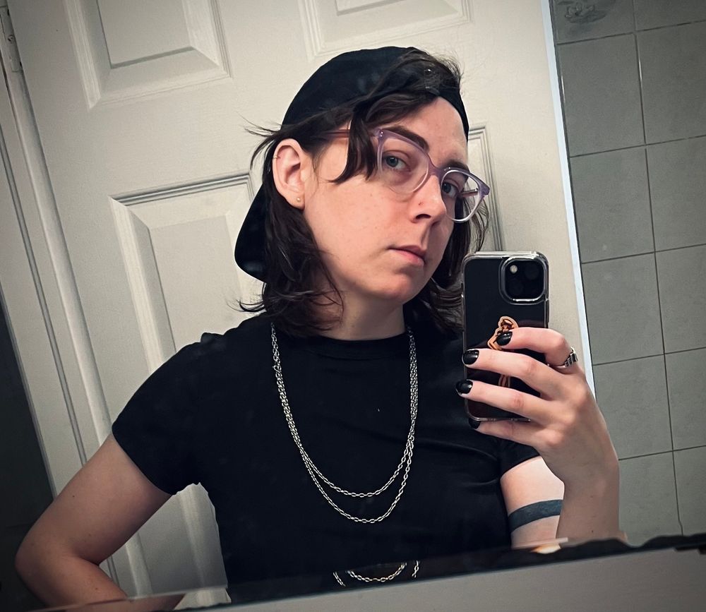 valérie in a black t shirt and backwards cap. wearing chains and nail polish