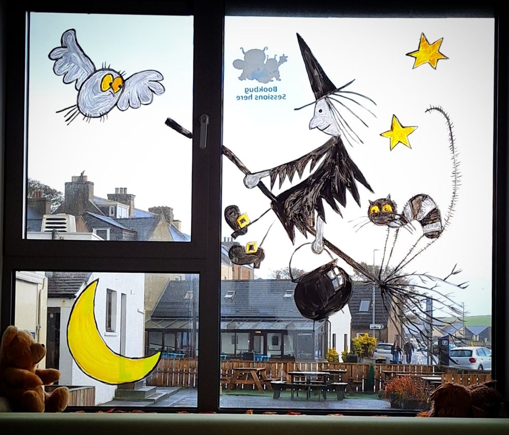A photo of a window painting of Meg and Mog. A witch on a broomstick, a cat, an owl and a moon and stars
