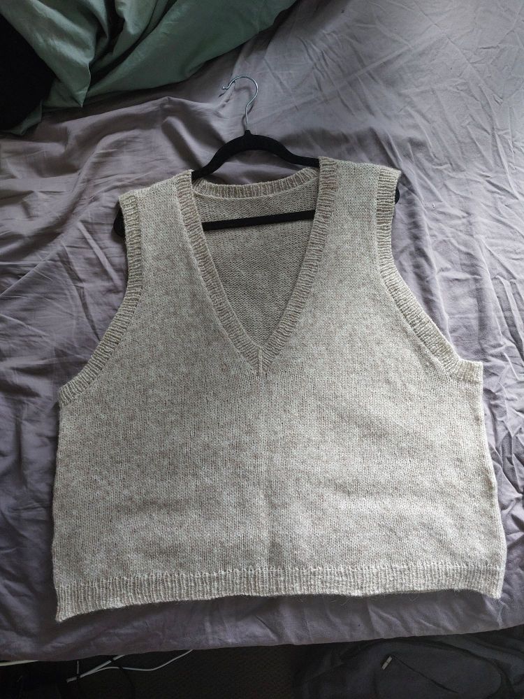 a flatlay of a hand knit sweater vest with a deep v neck. its made out of soft looking alpaca wool in a white-beige colour.