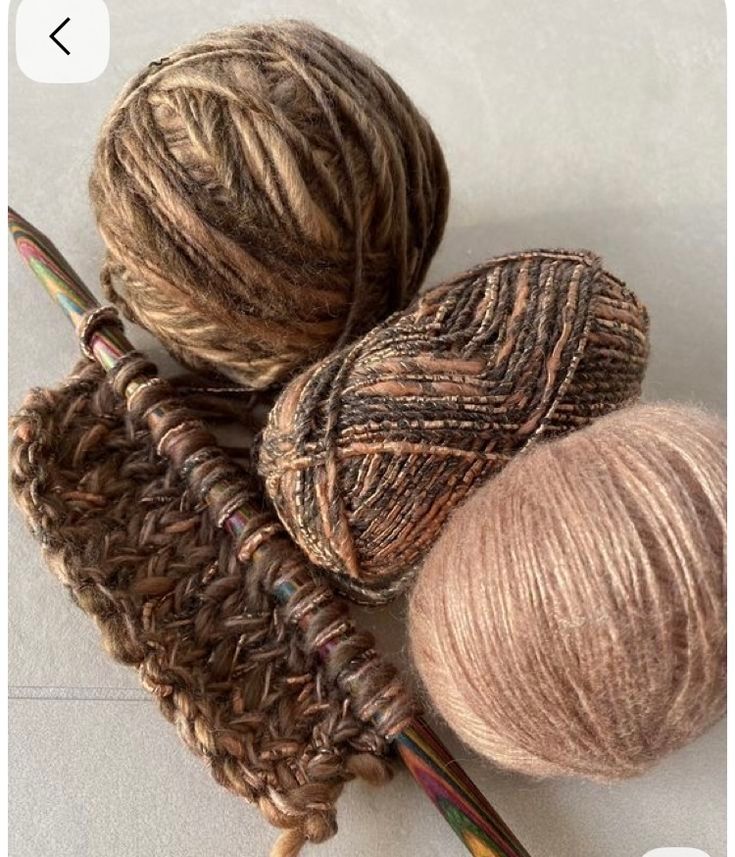 Stricknadeln mit ein paar Reihen abgestrickter Maschen. Daneben in drei Brauntönen, Wollknäule.