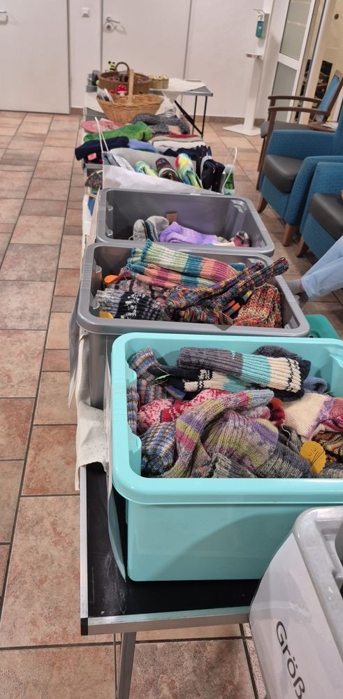 Blick auf die Verkaufstische. Man sieht viele gestrickte Socken in verschiedenen Größen, handgenähte Sitzkissen, Schals, Mützen und selbstgemachte Marmelade 