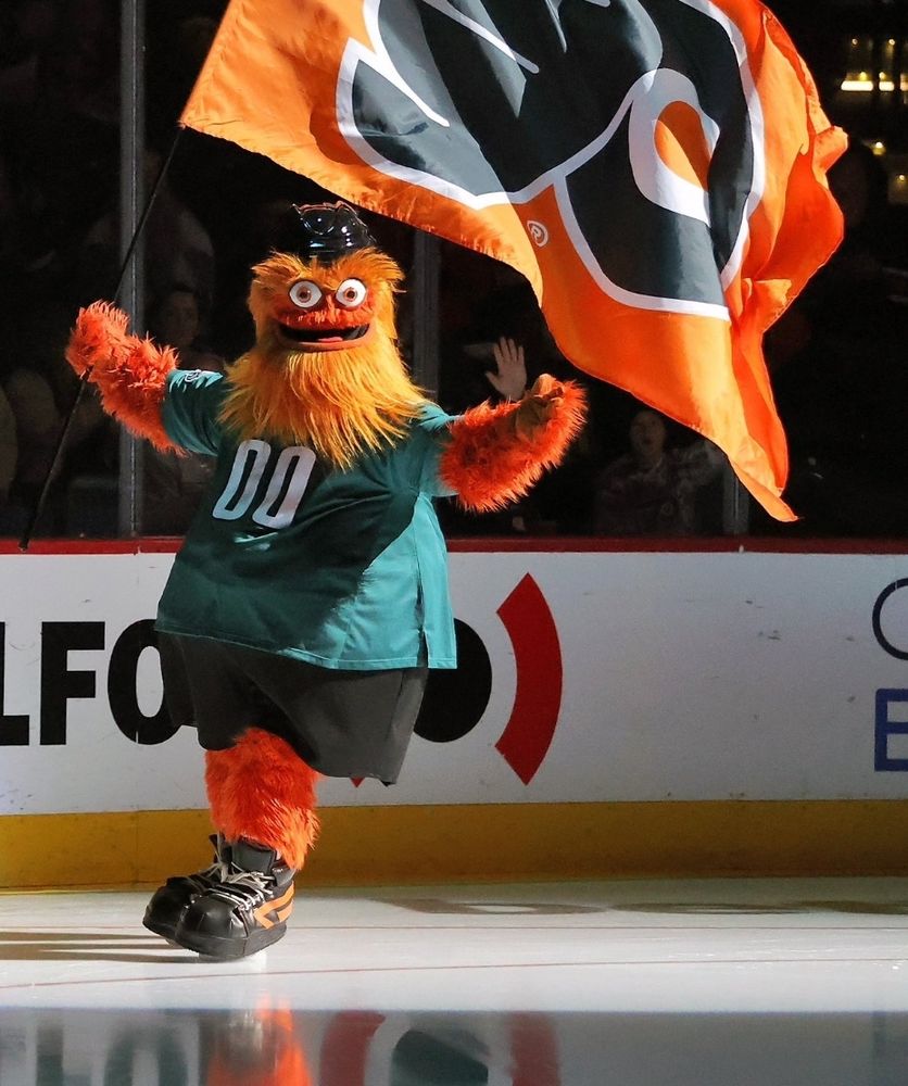 Gritty, the unhinged hockey mascot, in an Philadelphia Eagles jersey ice skating with a Philly Flyer flag