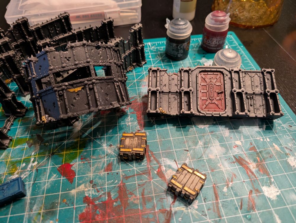 Various pieces of the Compound Siege (ruin walls, boxes, etc.) terrain set painted silver with various details of red and gold. 