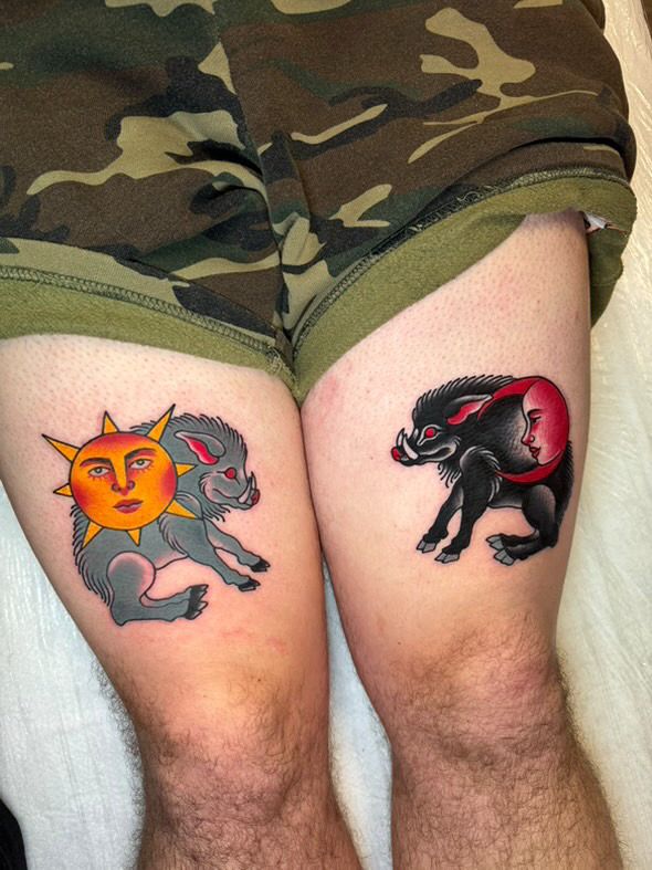 Two thigh tattoos, both of boars, one grey overlaid with a sun motif, the other black with a moon motif.