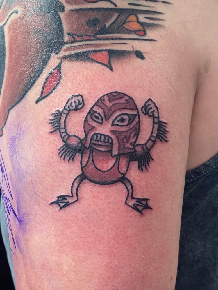 A small black-and-white tattoo of a frog wrestler wearing a mask reminiscent of the Creature from the Black Lagoon