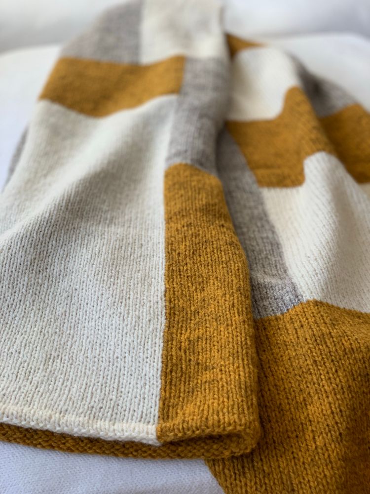 A knitted shawl with golden, gray, and natural white rectangles