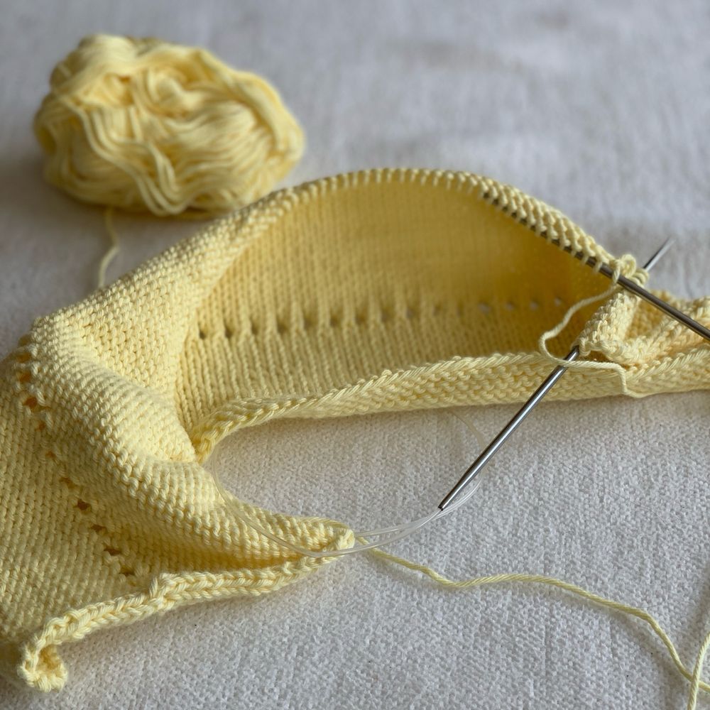 Knitting work in progress. A yellow stockinette fabric with a row of simple yarnovers