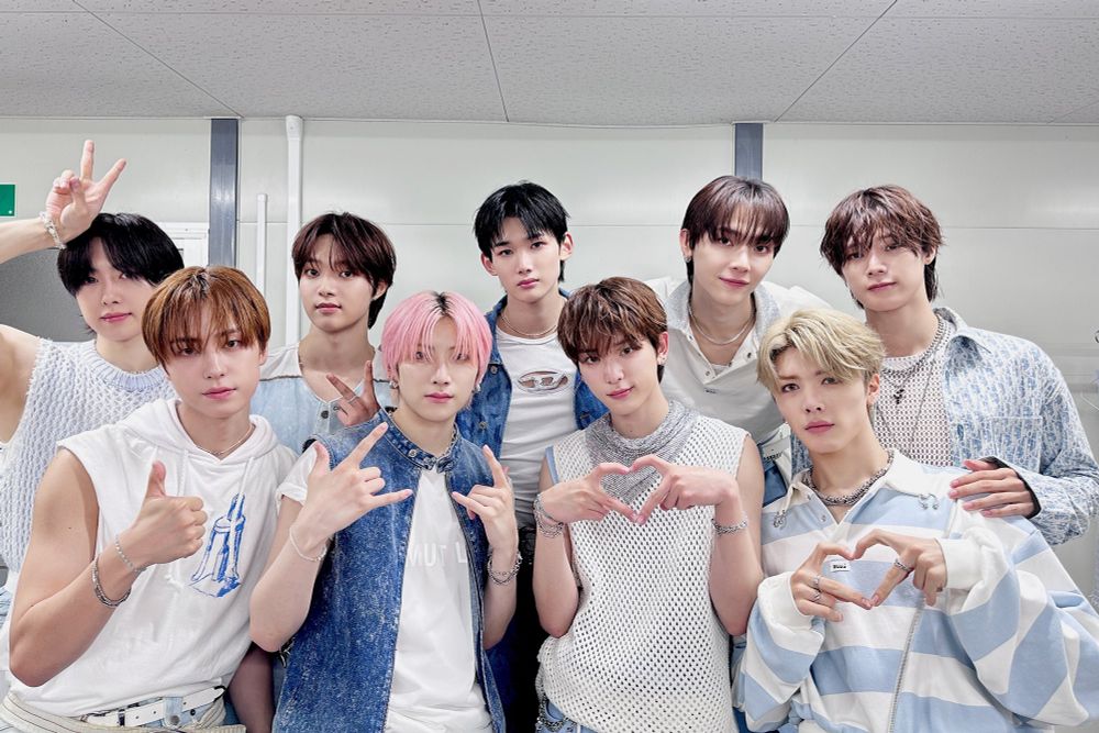 &Team backstage at Music Core. They're all wearing white or blue tops and are standing in their usual formation. Back row is Fuma, EJ, Jo, Nicholas, K. Front row is Taki, Yuma, Harua, Maki. Harua and Maki are making hearts with their hands.