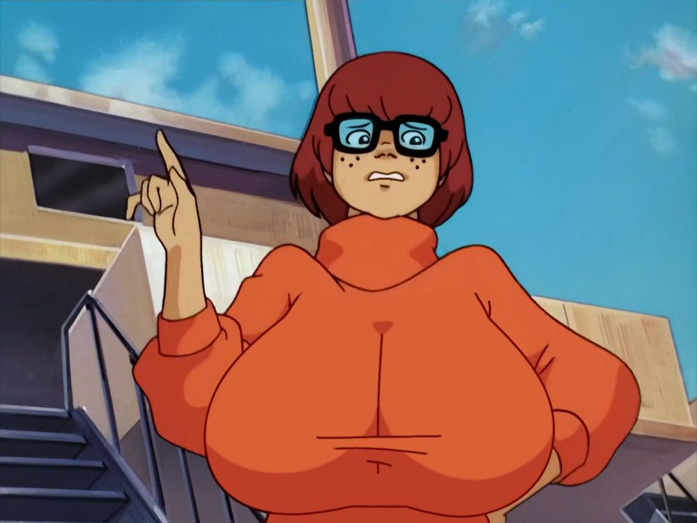 In the edited screenshot Velma has a much more unsure expression because off screen Daphne is trying to pinpoint what's different about her. She claims there's a glow- it must be something about her aura. Lacking her quartz crystals, she's forced to look through her fingers steepled into the shape of a diamond. As her friend's scan crosses her bust, Velma's about to nervously blurt out that her breasts have surged in size, but she holds her tongue while the oblivious Daphne turns her attention upwards to her hair. Velma breathes a sigh of relief and says "yup, secret's out- new conditioner."