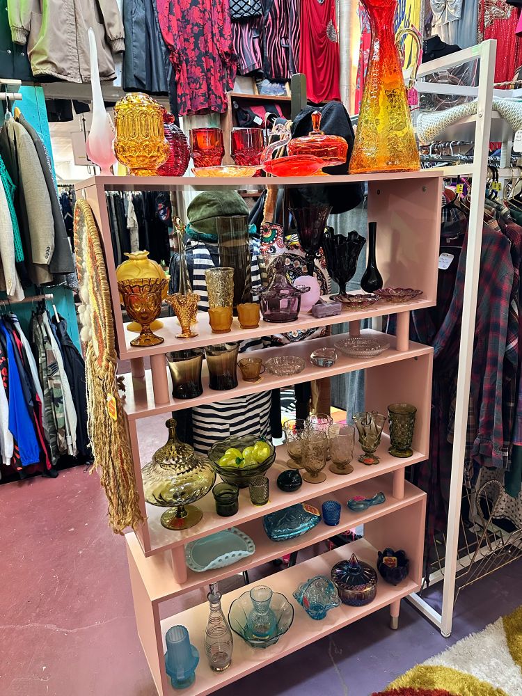 A pink 60s style shelf filled with rainbow collections of vintage glass