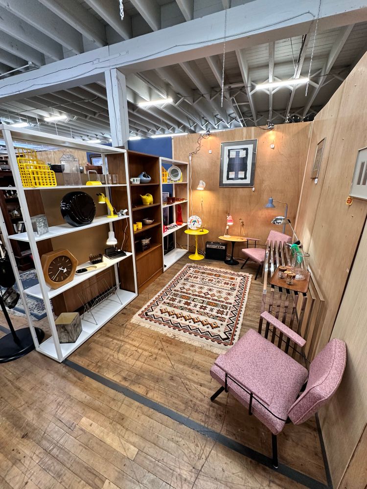 A space in a vintage vendor mall with wood walls and mid century modern shelving full of high-design trinkets, lamps, and furniture. The space is new so it's not completely full yet.