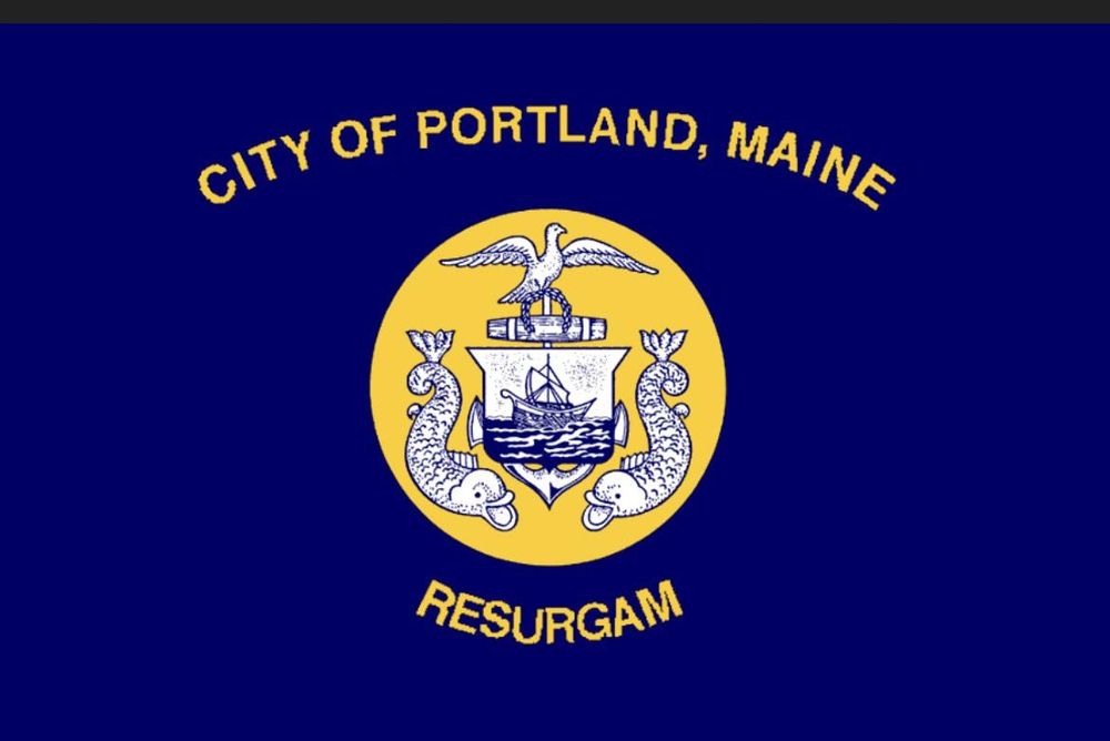 City of Portland Maine flag, an offbeat assemblage of eels, a seagull with peace wreath, and a sailing ship within a gold circle with the words "City of Portland Maine" in an arc above and "Resurgam" below. 
