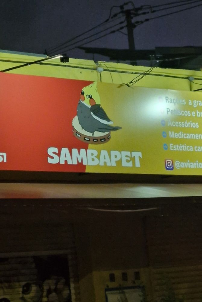 foto da fachada de um petshop chamado SAMBAPET à noite, a logo é o desenho de uma calopsita sentada em um pandeiro.