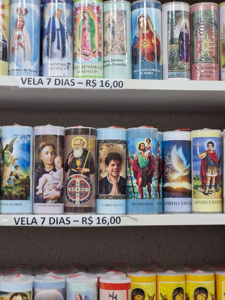 foto de prateleiras com velas de 7 dias de diversos santos, dentre eles, Carlos Acutis, o santo dos crônicamente online