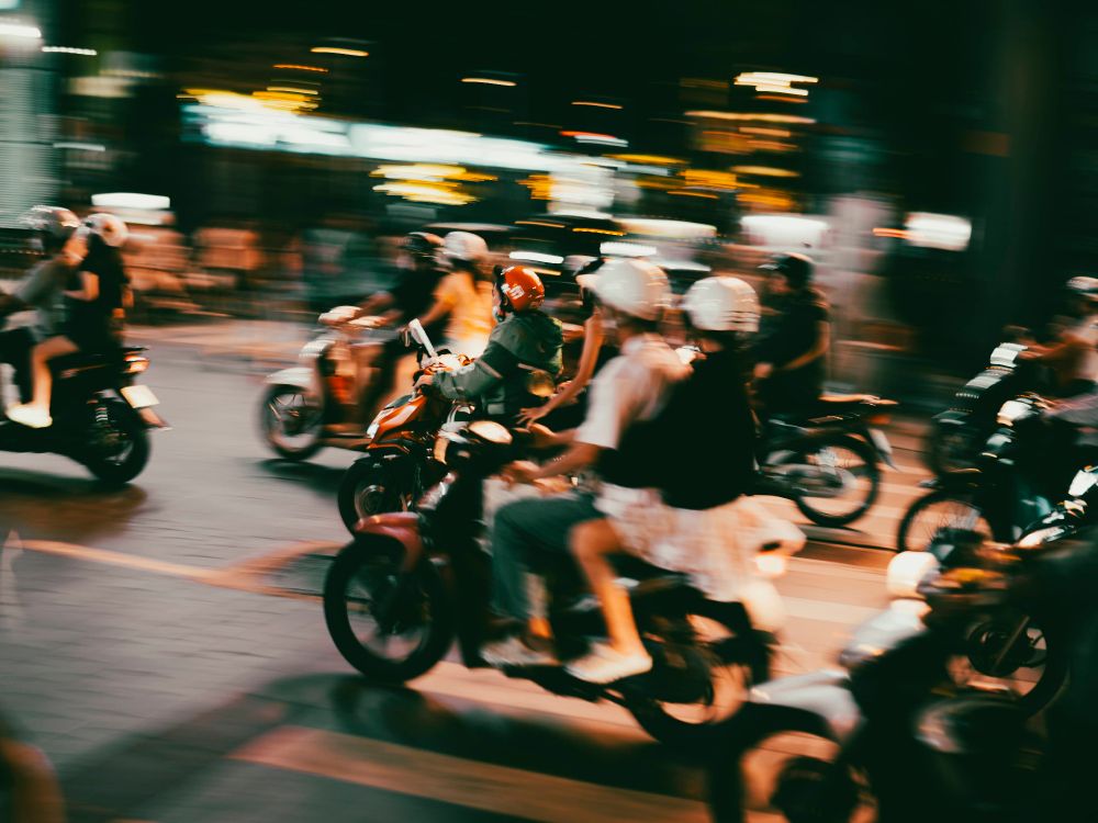 A pic of a bunch of people on scooters taking off from a red light in Hanoi. There's a single Grab driver in the middle, focused, the rest are in blurry motion