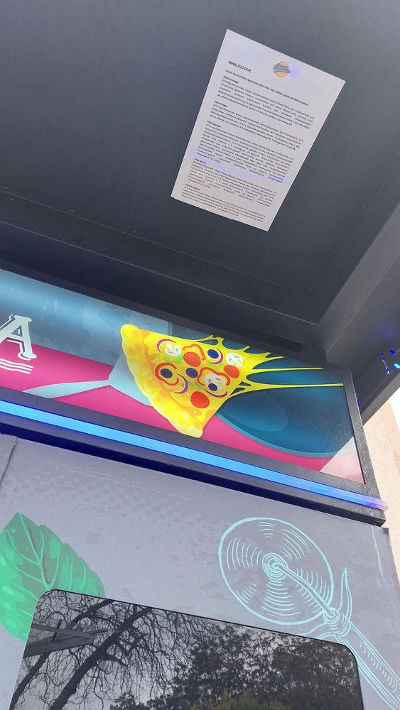 Zettel mit Zutaten für die Pizza unter das Vordach des Automaten geklebt.