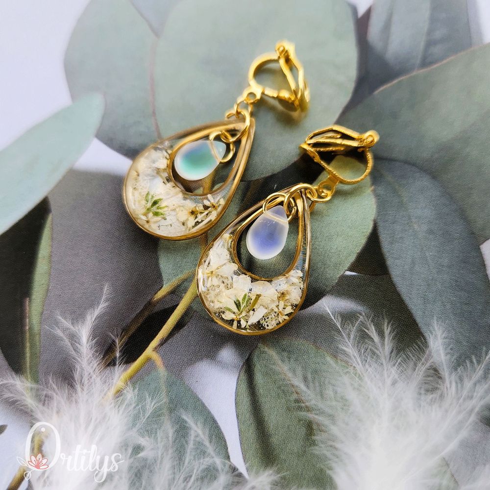 Des boucles d'oreilles en forme de goutte, dont le centre est creux pour y accueillir une perle en verre. Ici, les boucles sont dorées, les fleurs du contour sont blanches et la perle est couleur perle !