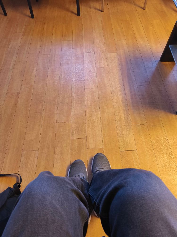 User sitzt im Wartezimmer. Blick aus seiner Perspektive, auf seine Knie und den Fußboden. 