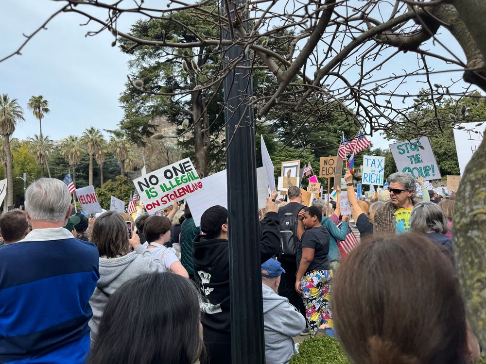 Crowd at CA capitol, Sacramento, with numerous signs “No one is illegal on stolen land” “stop the coup” “tax the rich” “No Elon” and “F-Elon” 