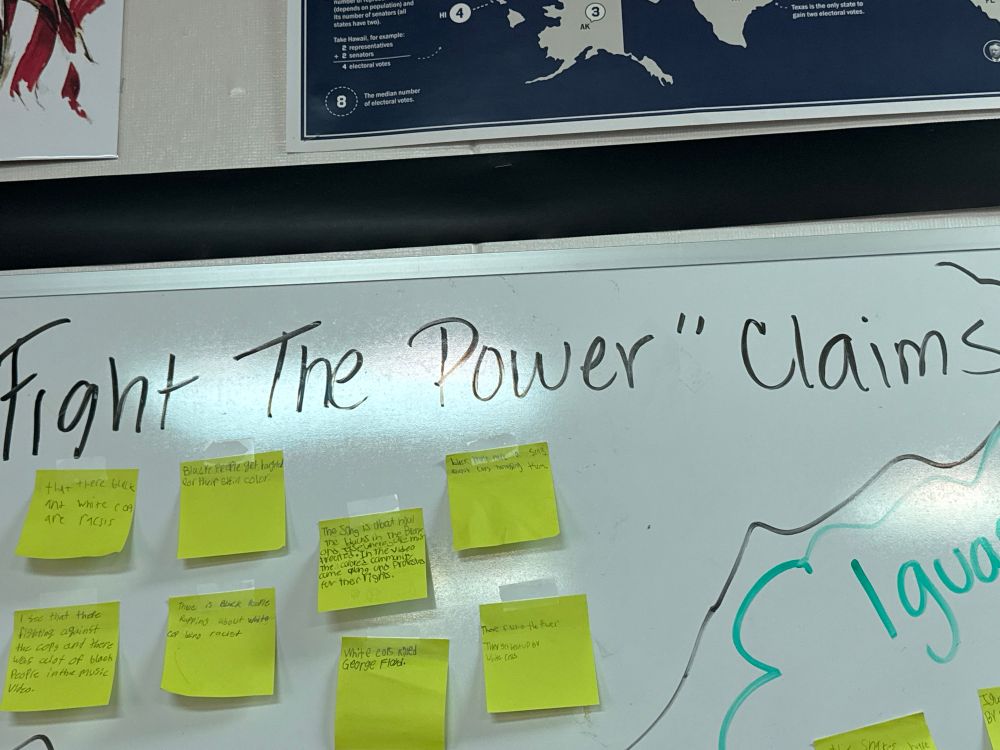 white board with “Fight the Power” claims and some student responses on Post it Notes. 