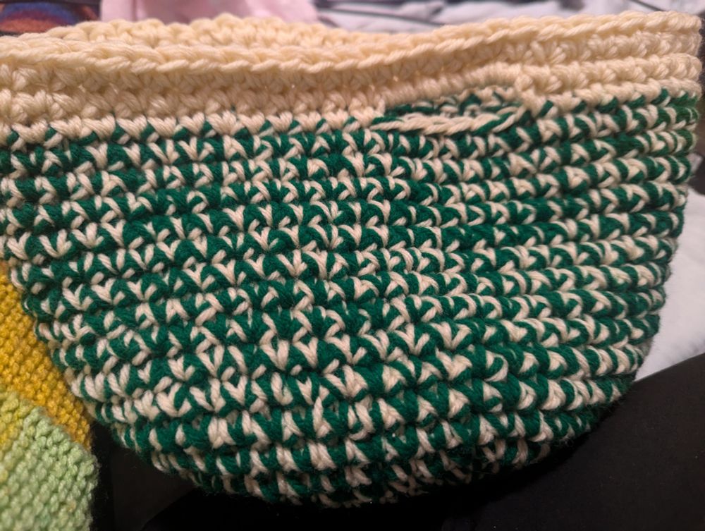 A crochet basket with one strand of green and one strand of off white yarn, with a solid off white top.