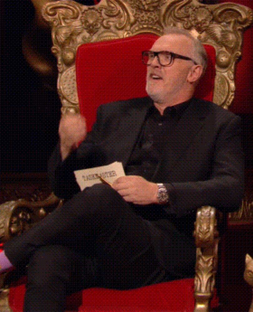 a man in a black suit is sitting in a red chair