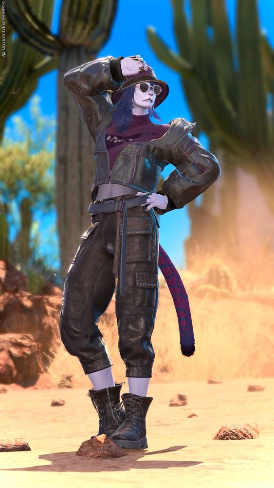 A screenshot of Teegan Irving, a player character in the game Final Fantasy 14. She is a light purple furred Hrothgar with fluffy blue hair and blue eyes, purple leopard spots, and short dark fangs. She is posing dramatically in a desert while wearing a cropped black leather jacket, a purple high necked top, cropped leather trousers, black ankle boots, and a black and purple hat with dark sunglasses 